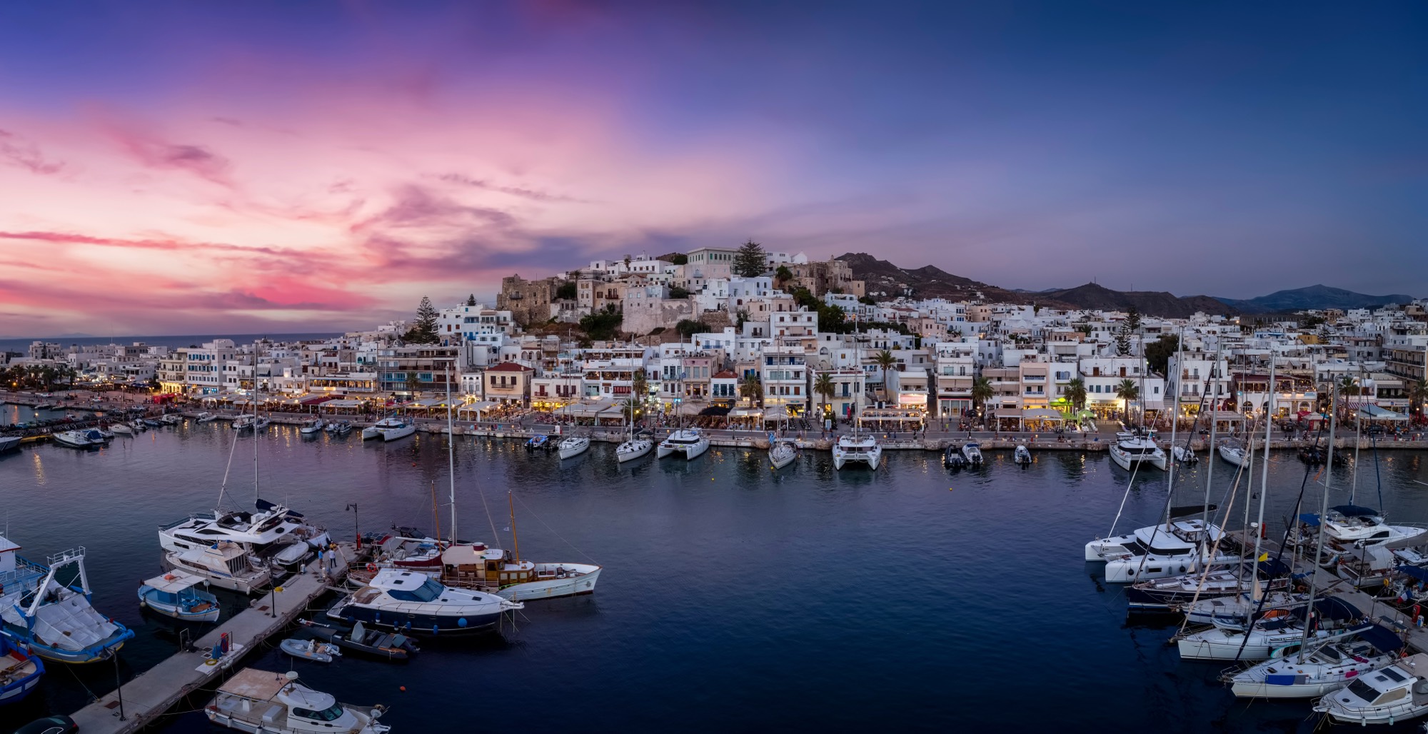 Le port de Naxos à l'heure bleue, les lumières de la ville se reflétant sur l'eau sombre.